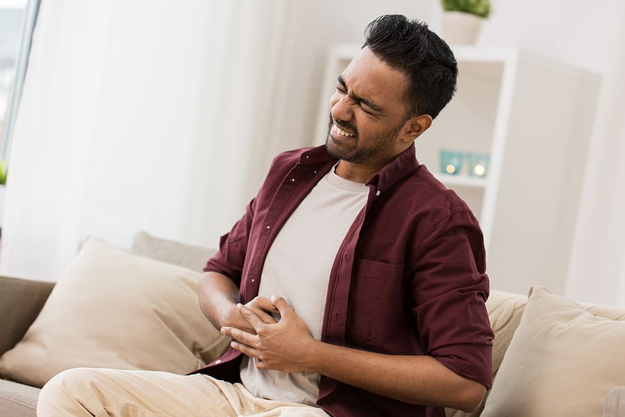 Man clutching stomach in pain while sitting on a couch