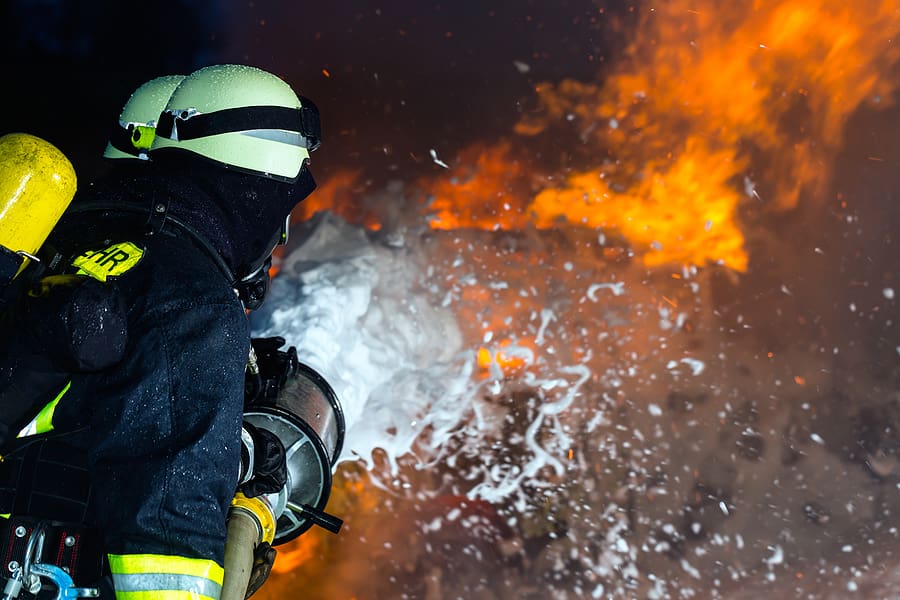 Firefighter spraying AFFF foam to extinguish a massive fire