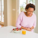 Veteran clutches her stomach in pain while eating breakfast due to a digestive problem