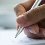 Close up of a veterans hand filling out paperwork for a VA disability claim