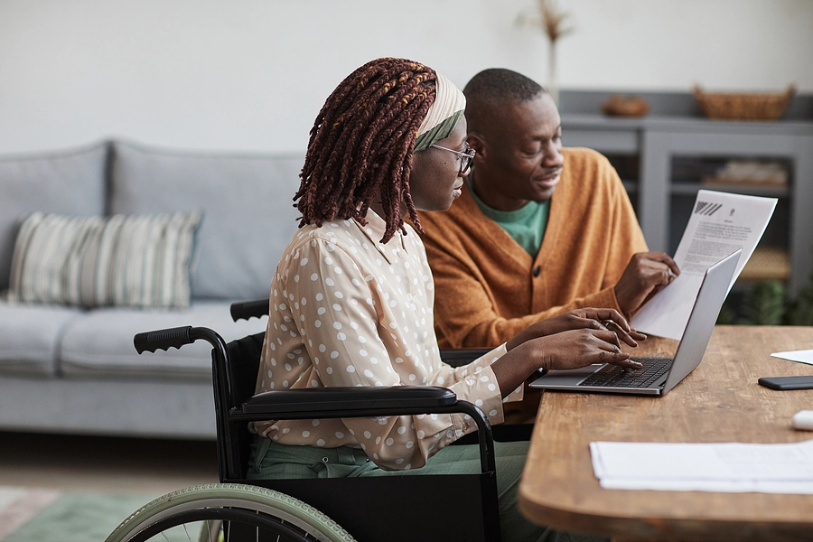 Husband and wife who is in a wheelchair checking the status of her VA claim on a laptop