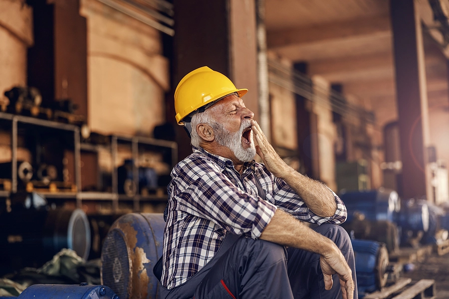 Older veteran wearing a construction hat yawning at work because he is tired due to sleep apnea