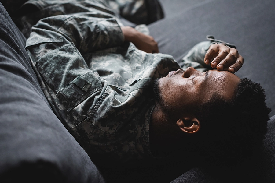 Young male veteran laying down on his couch with a debilitating migraine headache
