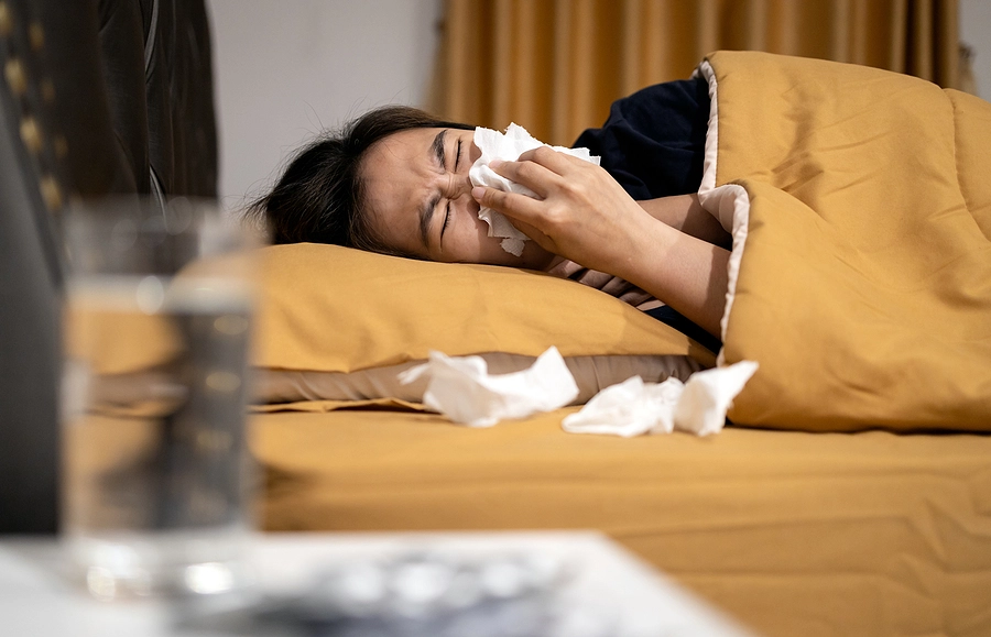 Young female veteran laying in bed with sinusitis surrounded by used tissues