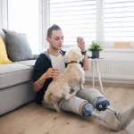 Double amputee veteran who is eligible for VA Special Monthly Compensation benefits sits at homme petting their dog