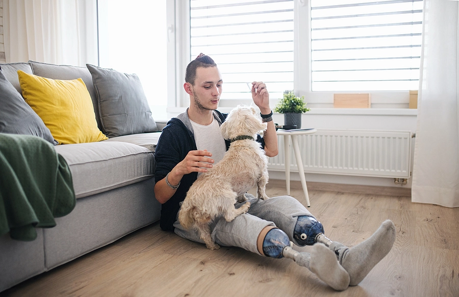 Double amputee veteran who is eligible for VA Special Monthly Compensation benefits sits at homme petting their dog