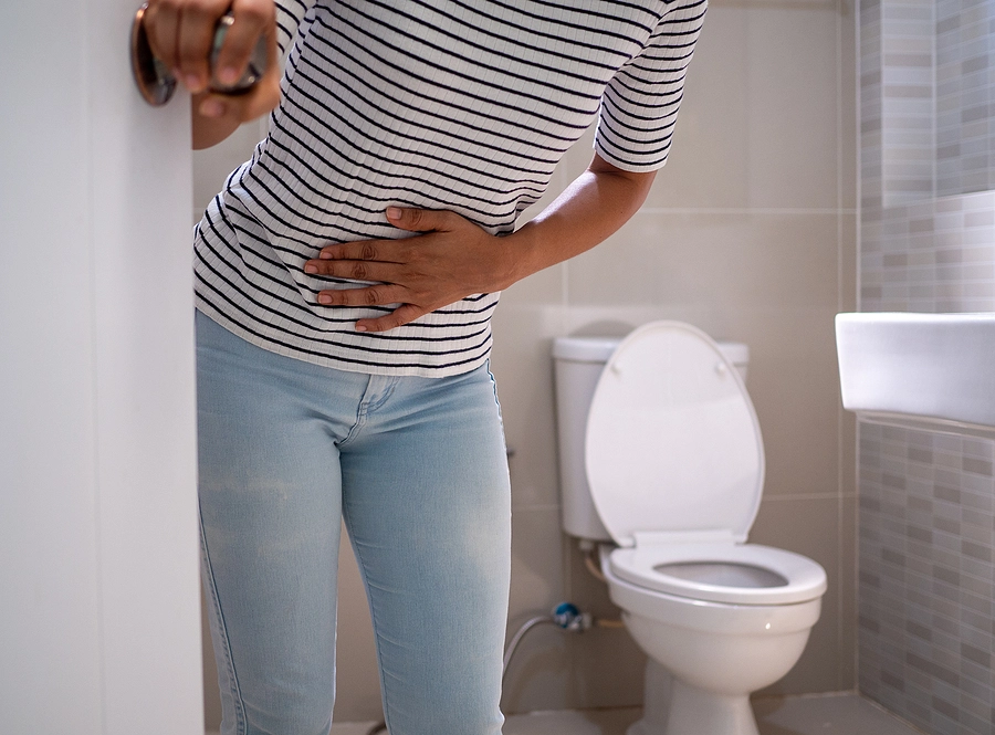 Female veteran with a gastrointestinal disorder clutches her stomach in pain after using the bathroom