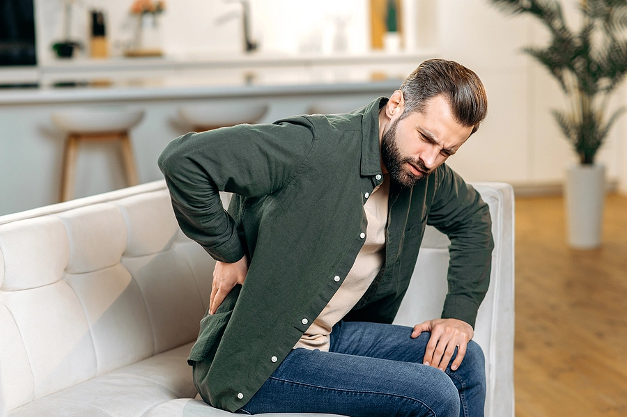 veteran with a sciatica va rating places his hand on his back as he tries to stand up from his couch